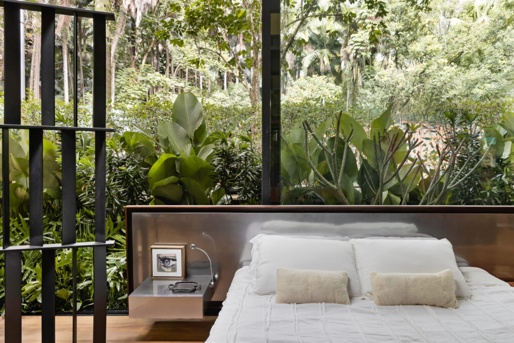 Cama da Casa Limiar R com cabeceira em aço inox diante de pano de vidro voltado para a vegetação