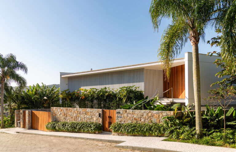 Fachada frontal de residência contemporânea com muro de pedra, portão de madeira e volumes brancos, com esquadrias Weiku