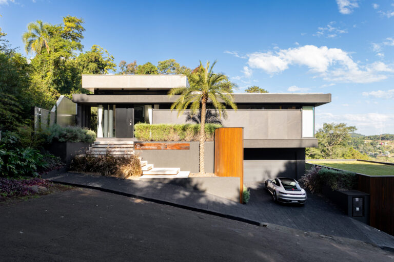 Fachada de acesso de residência contemporânea com beirais marcados, portão de madeira e esquadrias Weiku