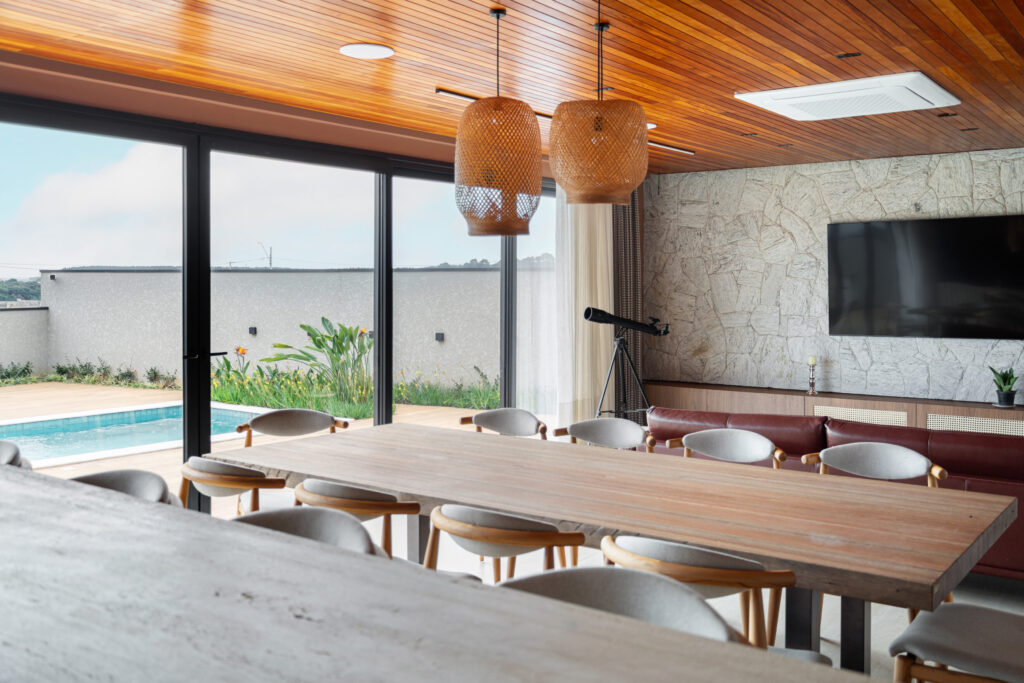 Espaço gourmet com forro de madeira, parede de pedra e esquadrias de vidro de correr Weiku abrindo para a piscina