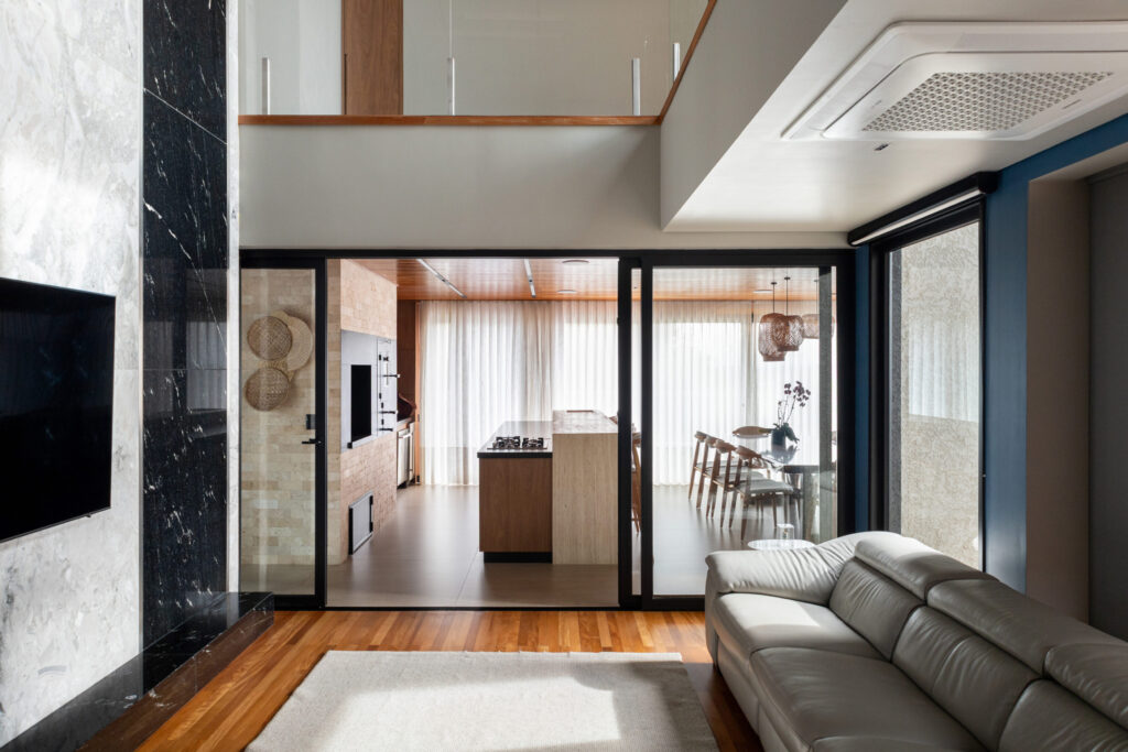 Living com painel de mármore preto e esquadrias de vidro de correr Weiku integrando o ambiente à cozinha