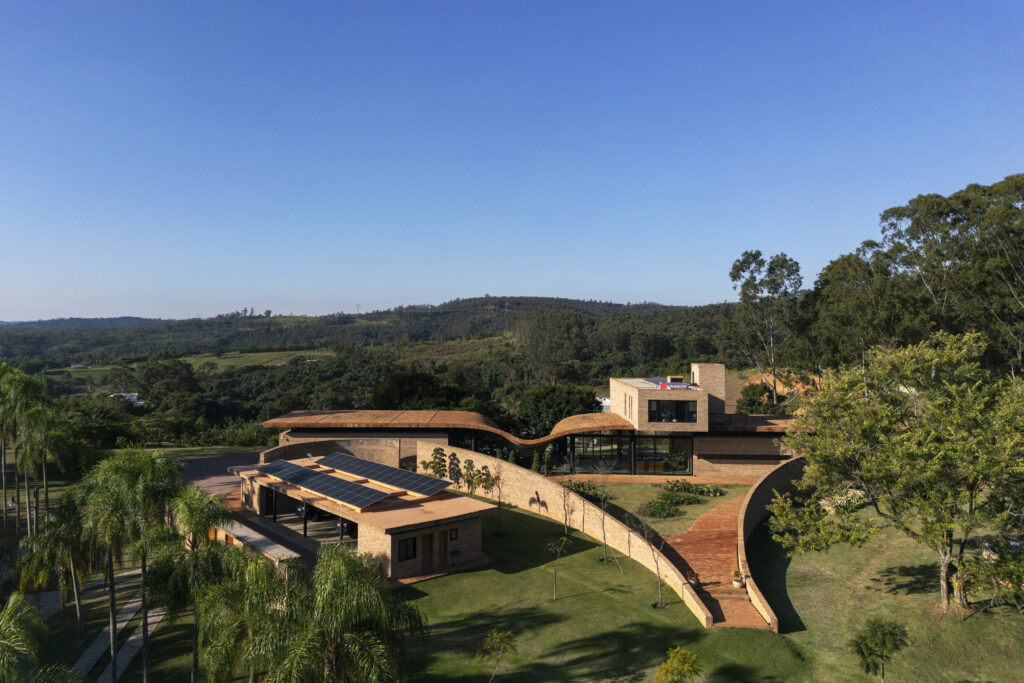 Vista aérea de residência de arquitetura orgânica com telhado ondulado em tijolo e esquadrias de vidro Weiku integradas à paisagem