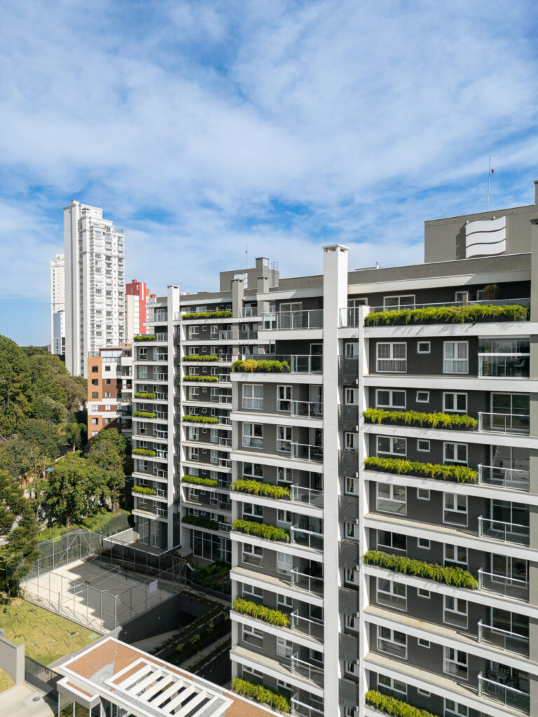 Vista aérea do Edifício Trebbiano com sacadas ajardinadas, guarda-corpos de vidro e quadra esportiva