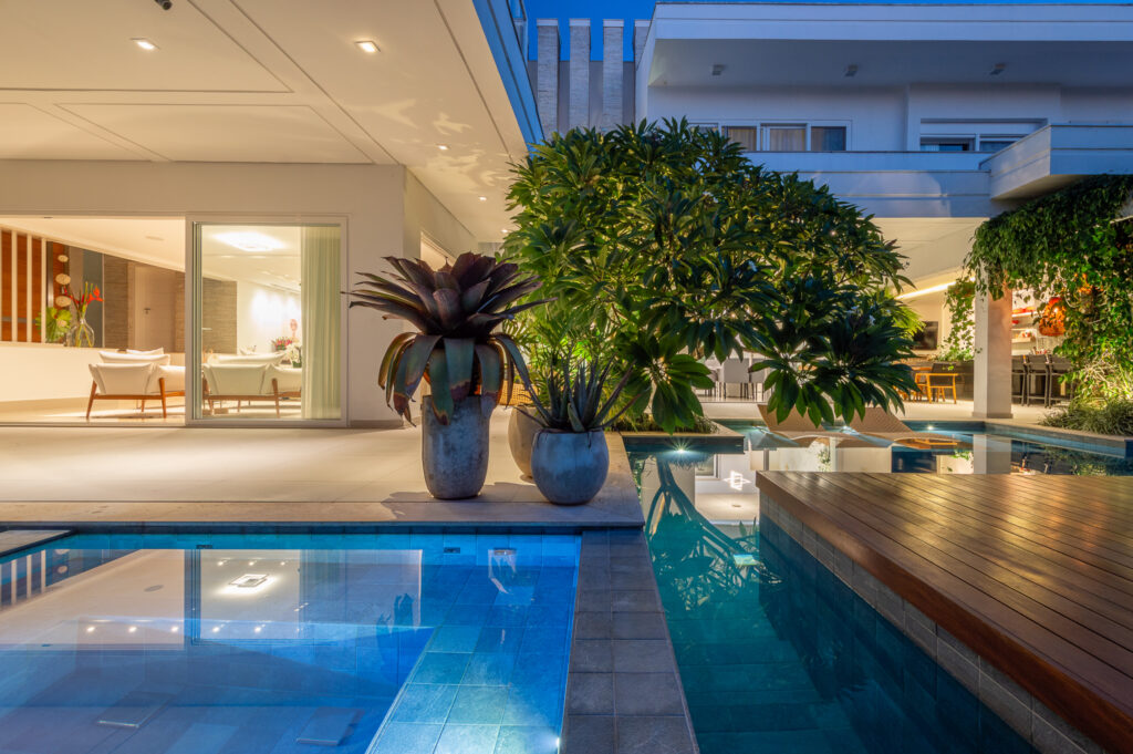 Piscinas iluminadas à noite com deck de madeira, diante de portas de vidro de correr Weiku abertas para o living