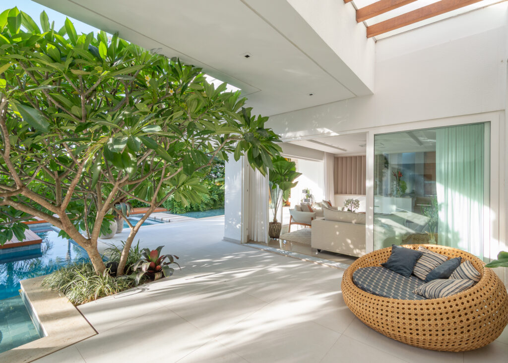 Varanda com árvore e piscina integrada ao living por portas de vidro de correr Weiku de perfil branco