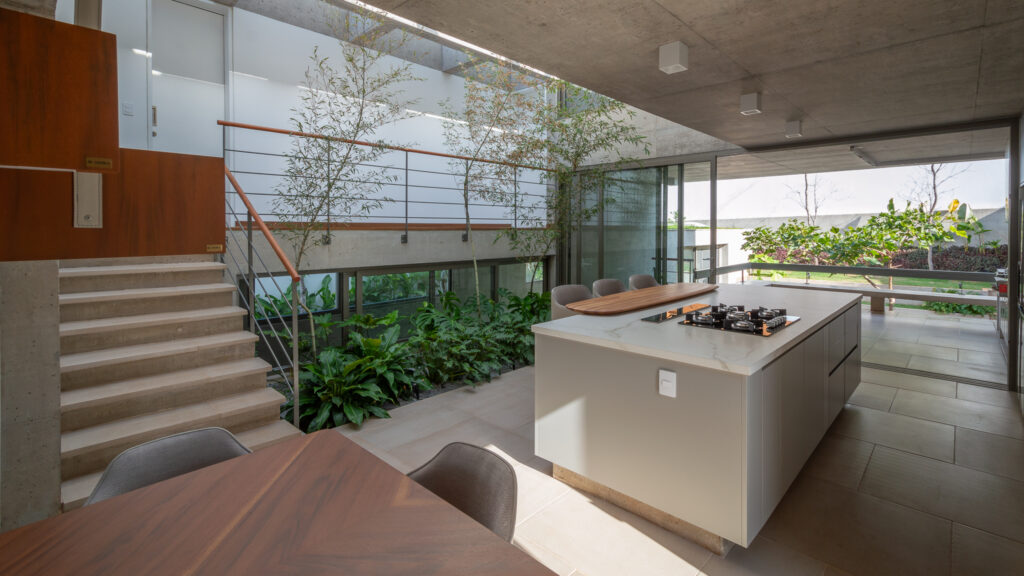Cozinha e jantar integrados ao jardim interno, com escada de concreto e panos de vidro Weiku ao fundo