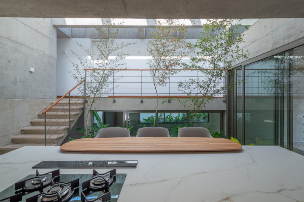 Jardim interno com árvores sob claraboia, ao lado de escada de concreto e esquadrias de vidro Weiku