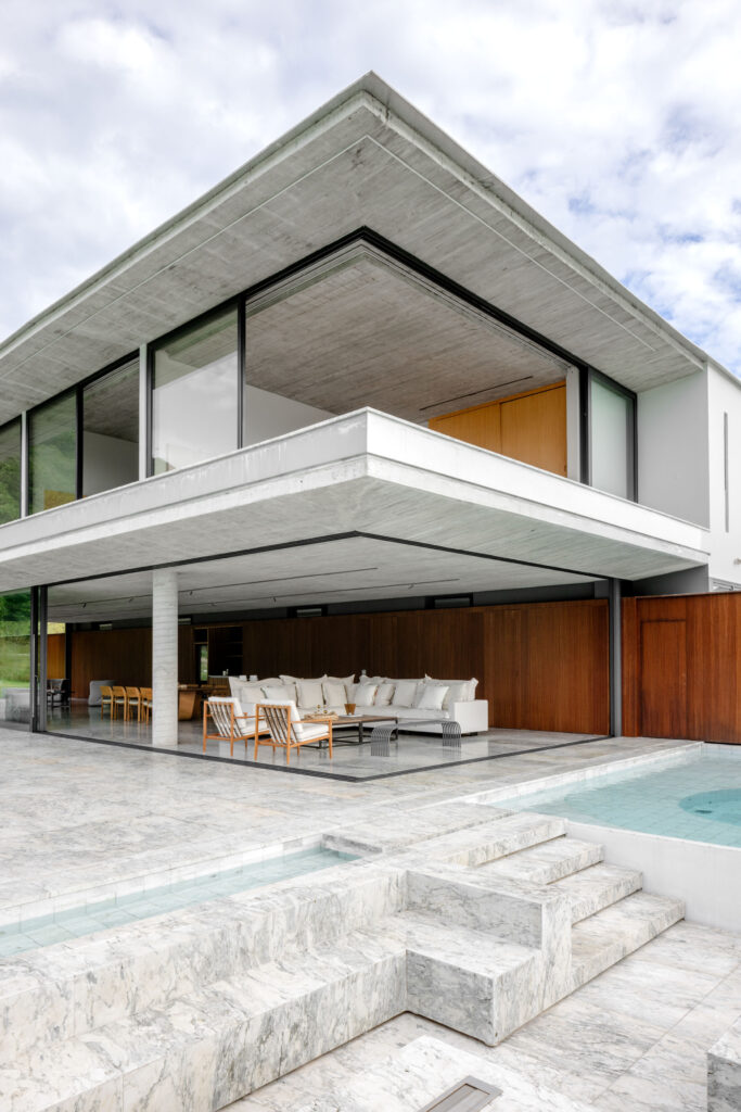 Canto da residência com portas de vidro de correr Weiku totalmente recolhidas, integrando o living ao deck de mármore e à piscina