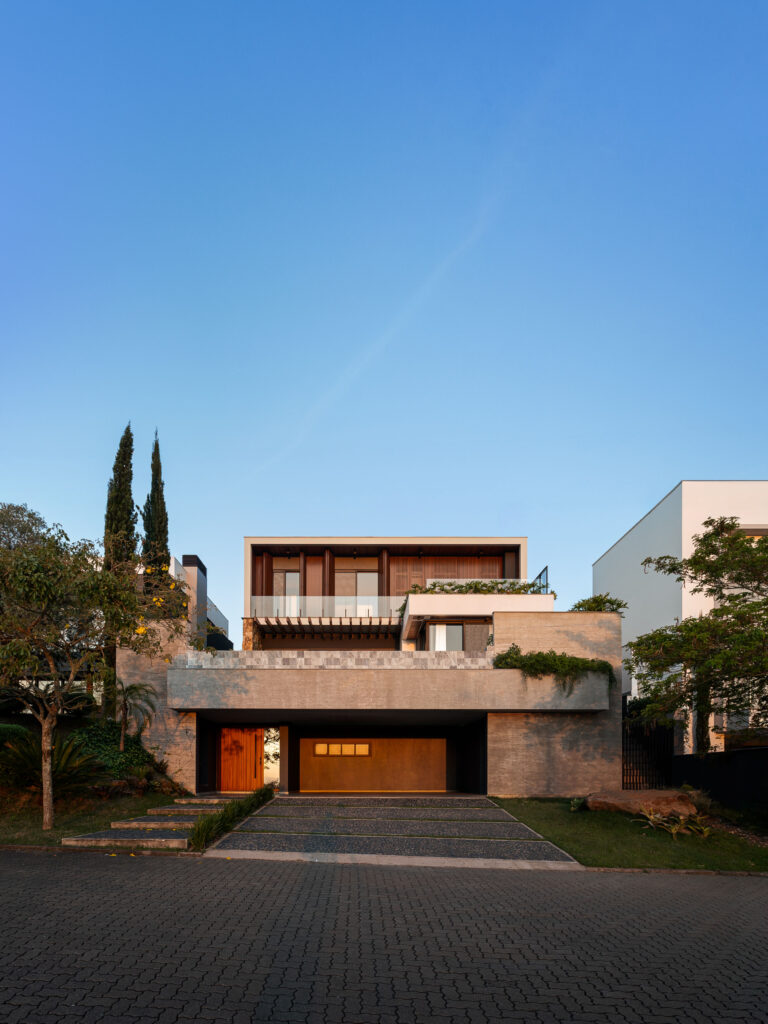 Fachada frontal de residência contemporânea em três níveis com pedra cinza, brises de madeira, pergolado e esquadrias Weiku