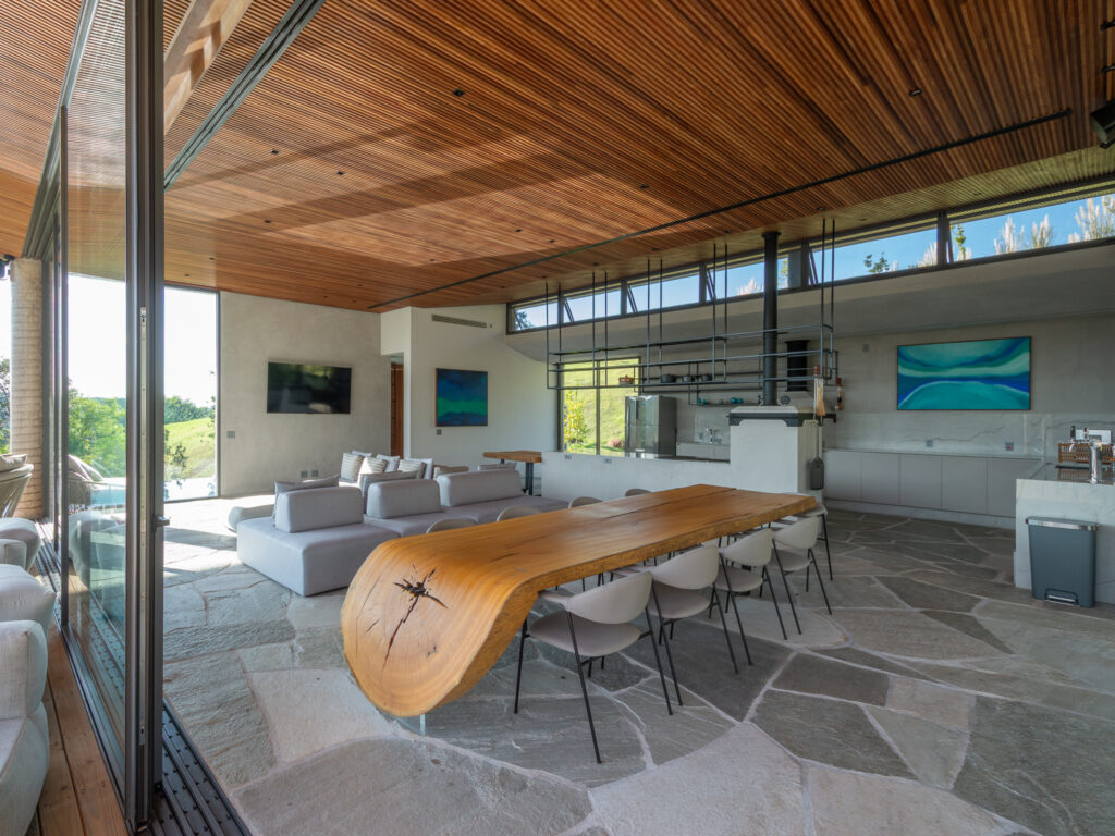 Espaço gourmet com mesa de madeira maciça, piso de pedra e portas de vidro de correr Weiku abertas para o deck