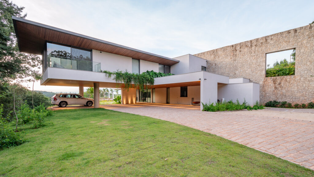 Fachada de acesso com volume em balanço, beiral com forro de madeira, muro de pedra e panos de vidro Weiku