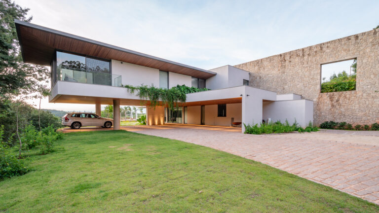Fachada de acesso com volume em balanço, beiral com forro de madeira, muro de pedra e panos de vidro Weiku