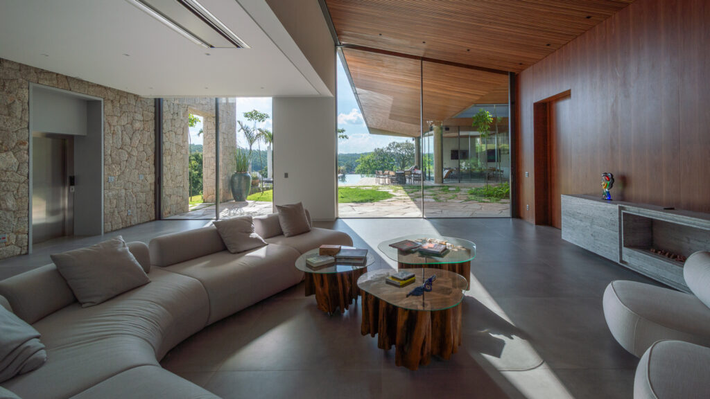 Living com parede de pedra, painel de madeira e pano de vidro Weiku de canto voltado para o jardim e a piscina