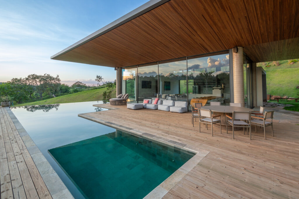 Piscina de borda infinita e deck de madeira junto ao espaço gourmet envidraçado com esquadrias Weiku de piso a teto