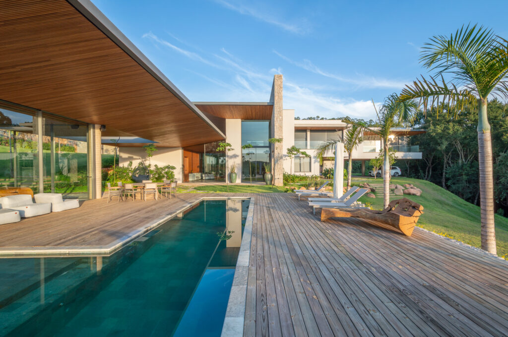 Piscina com deck de madeira diante do espaço gourmet com panos de vidro Weiku sob beiral de madeira
