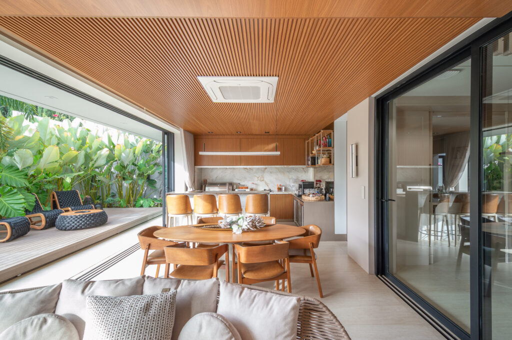 Espaço gourmet com forro ripado de madeira, aberto para o deck e o jardim por portas de vidro de correr Weiku de perfil preto