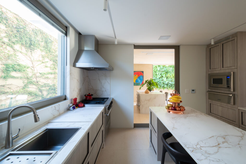 Cozinha com bancada de mármore e ampla janela de vidro Weiku voltada para muro verde