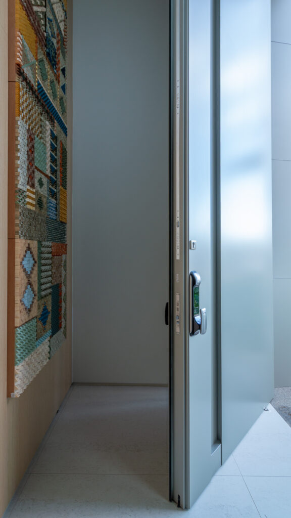 Hall de entrada com porta pivotante de grande altura e painel artístico em madeira colorida