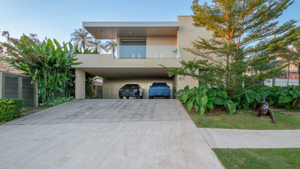Fachada frontal de residência contemporânea com volume em balanço sobre a garagem, sacada de vidro e paisagismo tropical