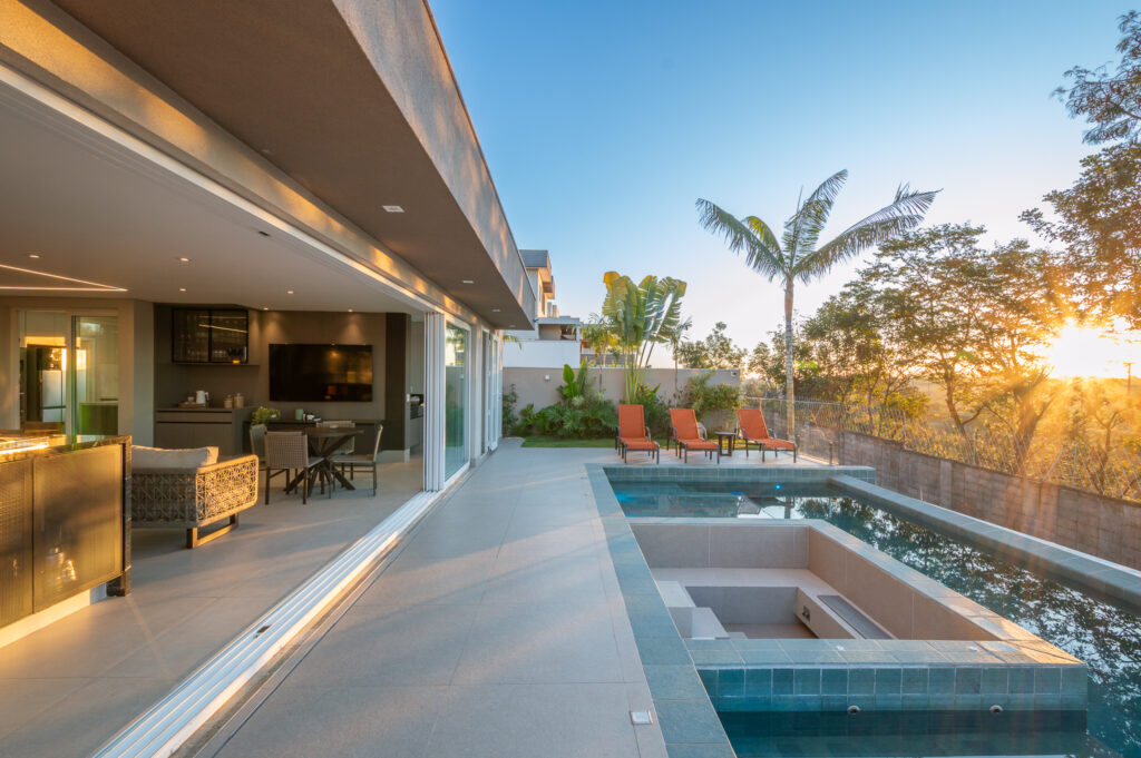 Varanda e piscina ao pôr do sol, com portas de vidro de correr Weiku abertas para o espaço gourmet