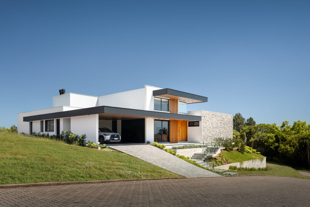 Fachada de residência contemporânea com volumes brancos, beirais escuros, parede de pedra rústica e esquadrias Weiku de perfil preto