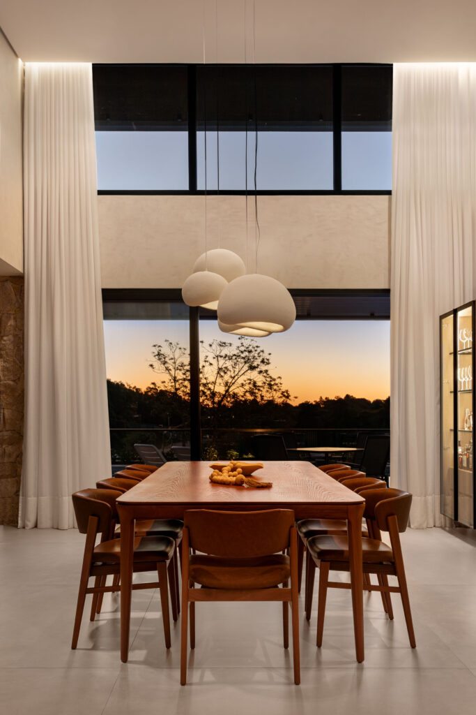 Sala de jantar de pé-direito duplo com janela alta e porta de vidro Weiku emoldurando o pôr do sol