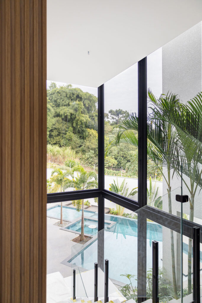 Escada com janela de canto de vidro Weiku de perfil preto emoldurando a piscina e a mata
