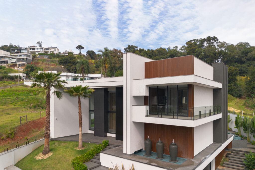 Residência contemporânea com painéis ripados de madeira, sacada de vidro e esquadrias Weiku em terreno de encosta