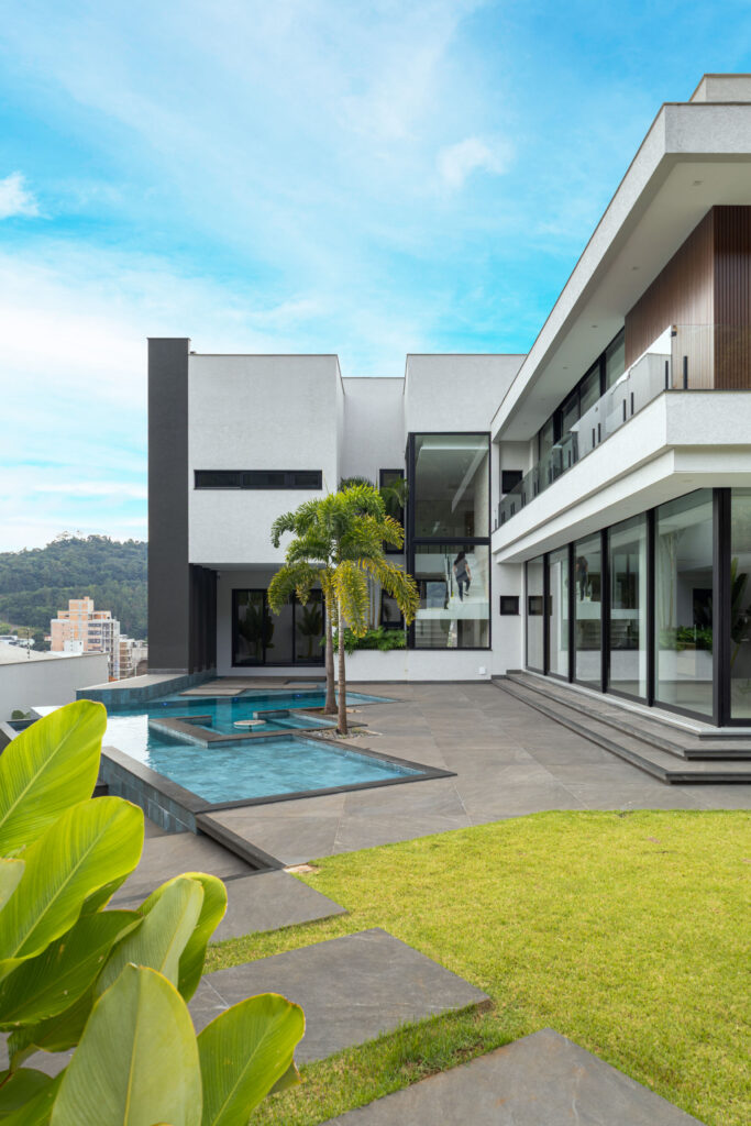 Fachada dos fundos com piscina recortada, escada envolvida por caixa de vidro e portas de correr Weiku de perfil preto