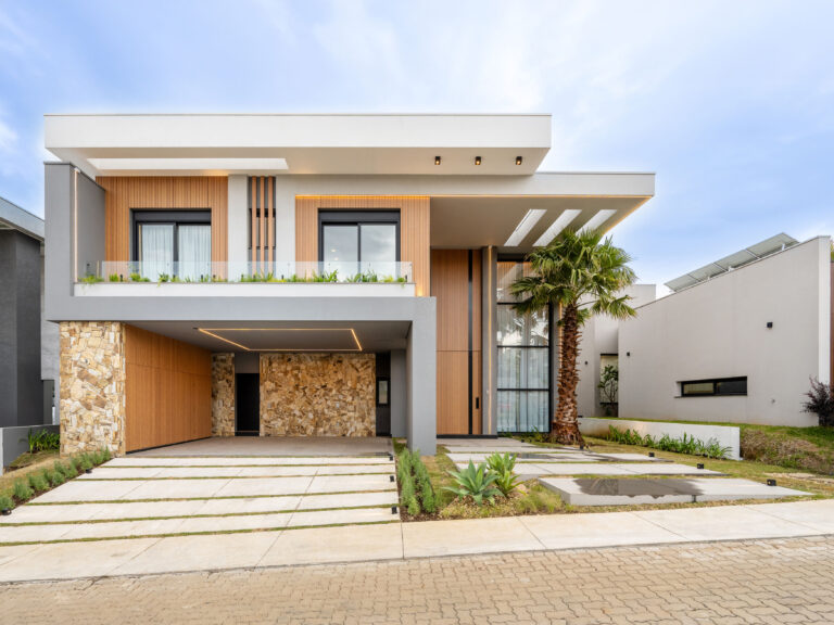 Fachada frontal de residência contemporânea com painéis ripados de madeira, pedra natural, sacada de vidro e esquadrias Weiku de perfil preto