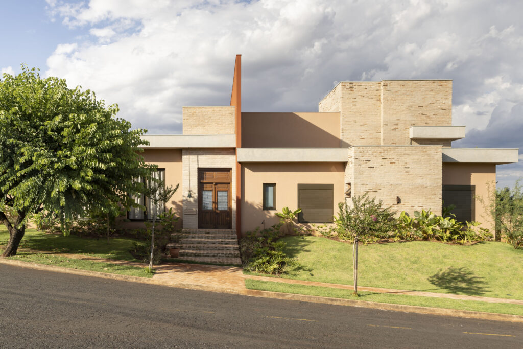 Fachada de residência contemporânea com volumes terracota, paredes de tijolo claro, plano vertical vermelho e porta de madeira