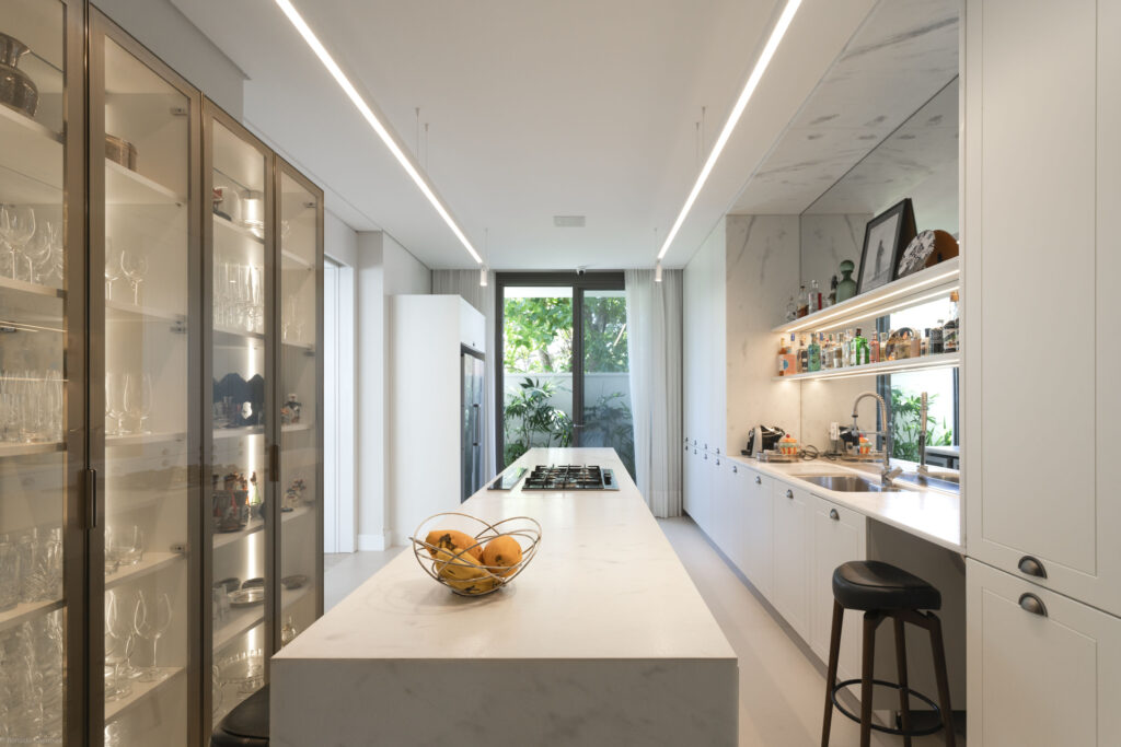Cozinha com ilha em pedra clara e porta de vidro Weiku de perfil escuro abrindo para o jardim