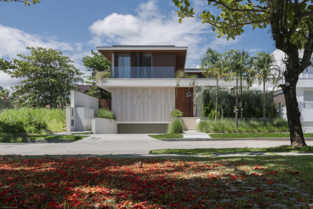 Fachada de residência contemporânea em travertino e madeira, com sacada de vidro e esquadrias Weiku no pavimento superior