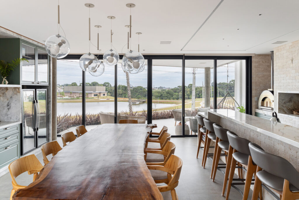 Espaço gourmet com mesa de madeira maciça e portas de vidro de correr Weiku de piso a teto com vista para o lago