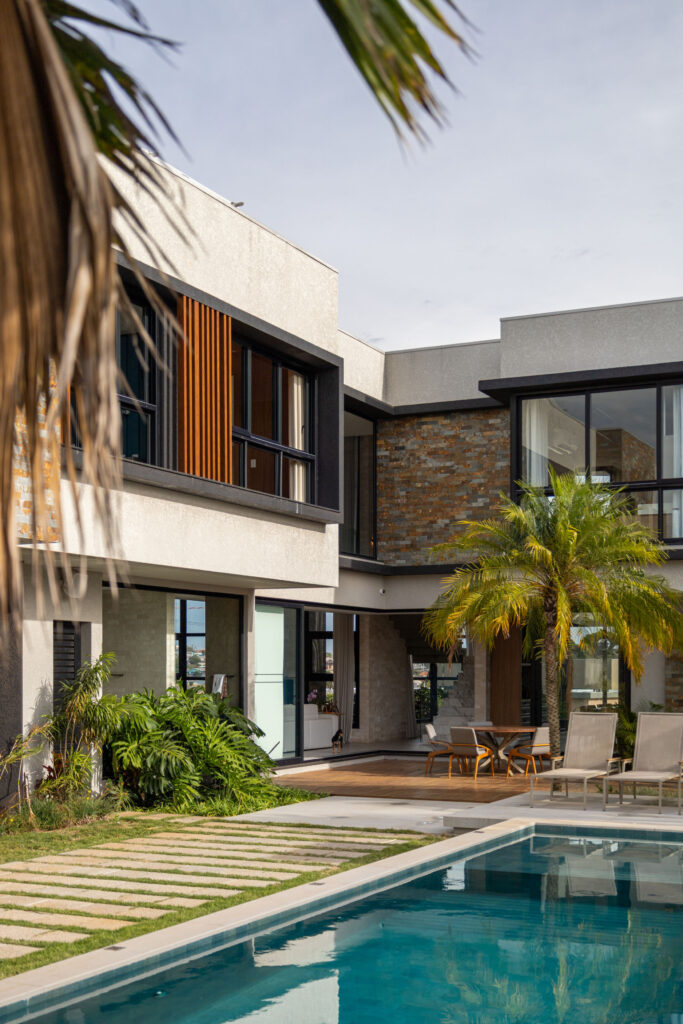 Fachada dos fundos com piscina, revestimento em pedra, brise de madeira e esquadrias de vidro Weiku de perfil preto