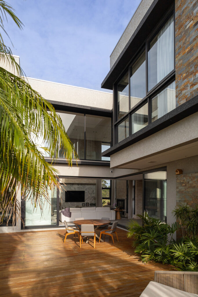 Varanda com deck de madeira integrada ao living por portas de vidro de correr Weiku totalmente abertas