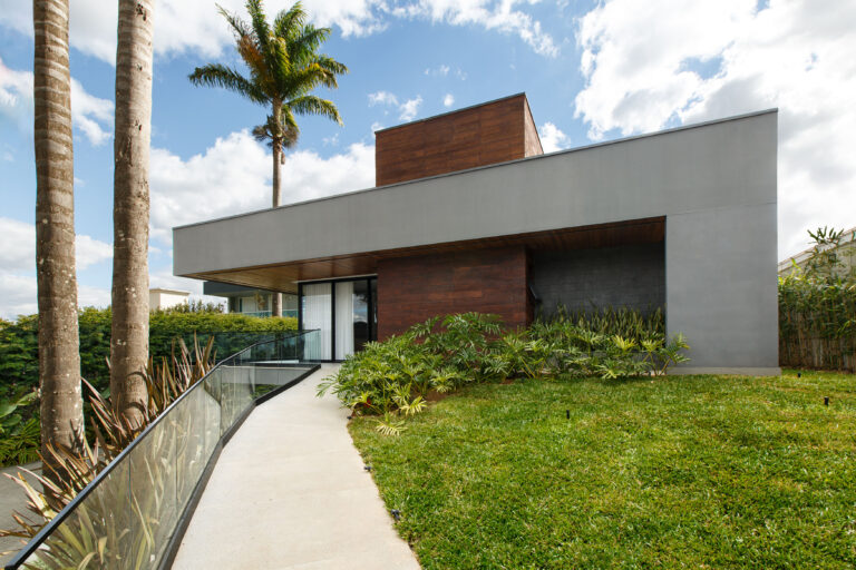 Fachada de acesso com volume cinza em balanço, revestimento em madeira, guarda-corpo de vidro e porta de vidro Weiku