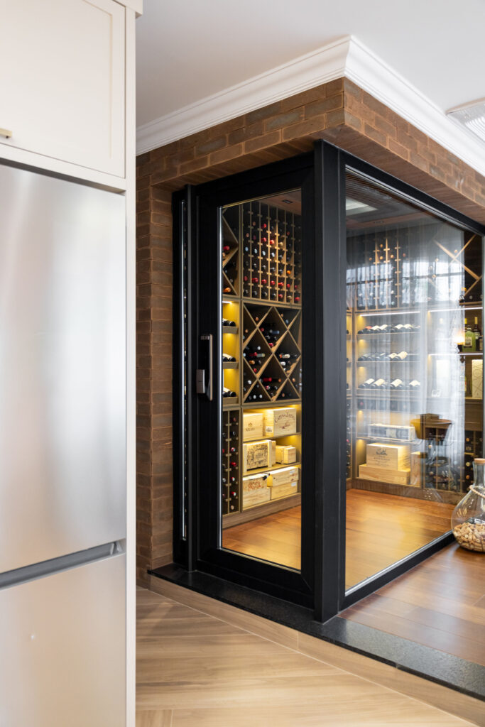 Adega climatizada com porta e painéis de vidro de perfil preto, revestimento de tijolo e prateleiras de vinho iluminadas