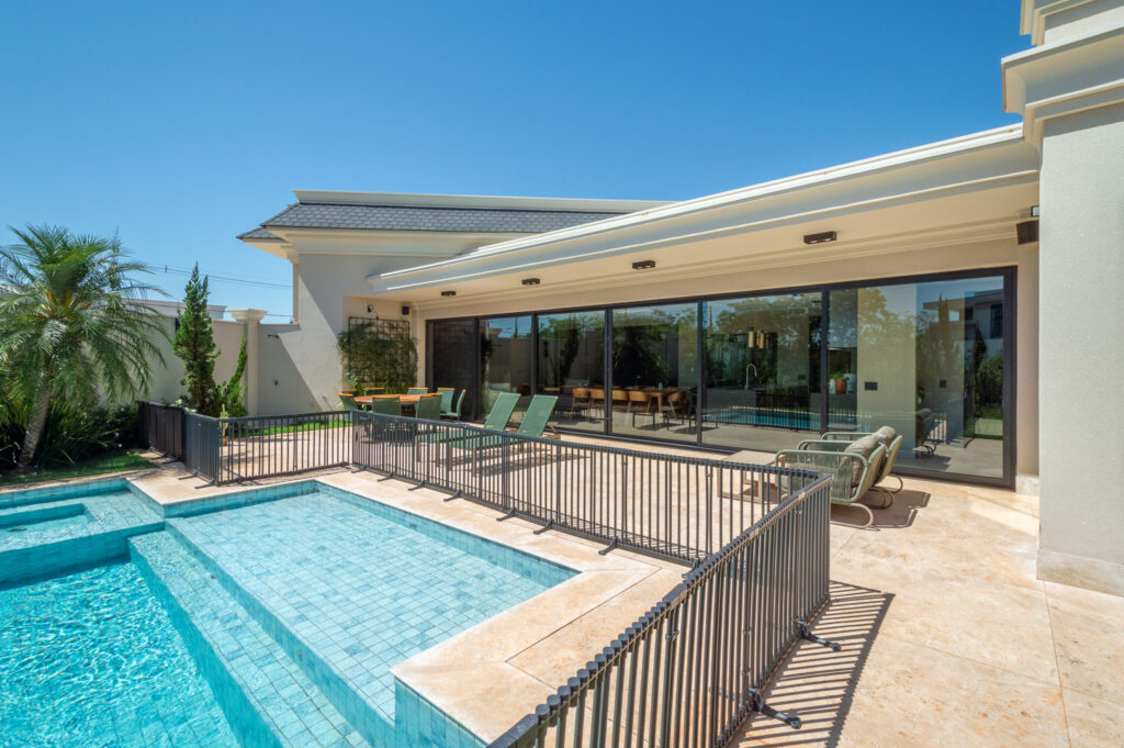 Piscina e varanda em travertino diante de panos de vidro Weiku de perfil preto na fachada dos fundos