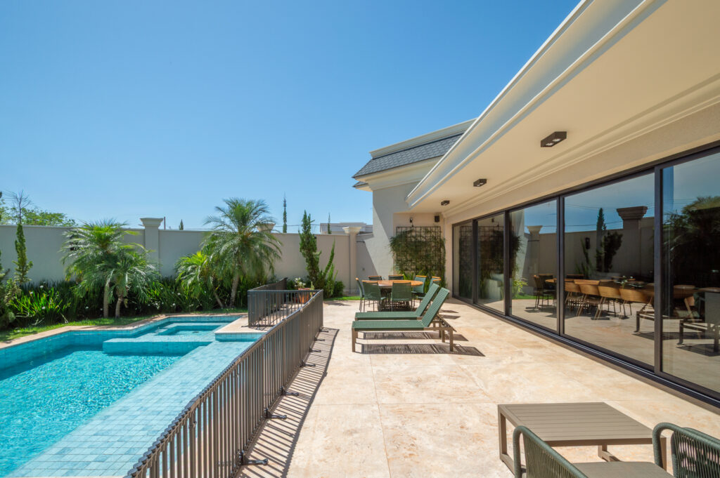 Varanda em travertino com espreguiçadeiras ao longo de portas de vidro de correr Weiku de perfil preto, ao lado da piscina