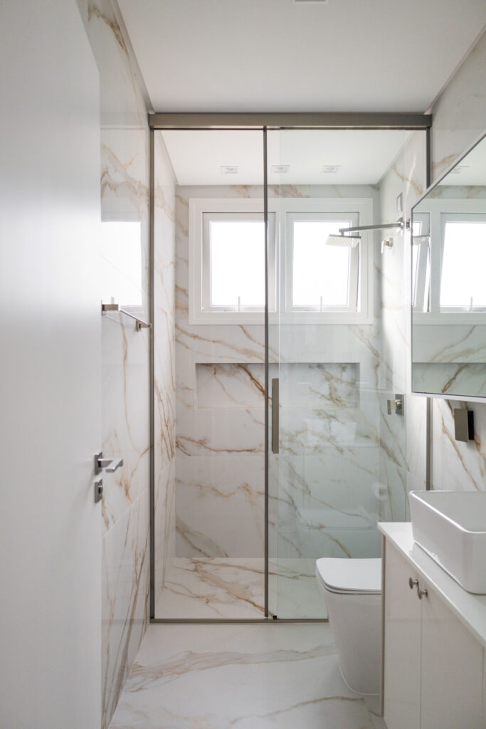 Banheiro em mármore com box de vidro e janela de vidro de perfil branco trazendo luz natural