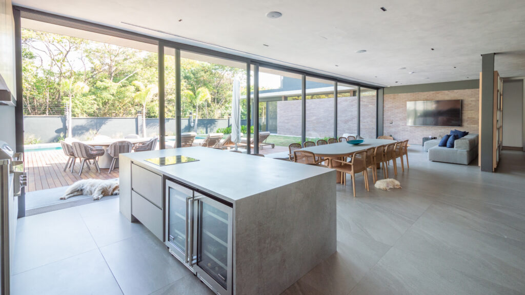 Cozinha com ilha integrada à sala de jantar, com portas de vidro de correr Weiku abertas para o deck e a piscina