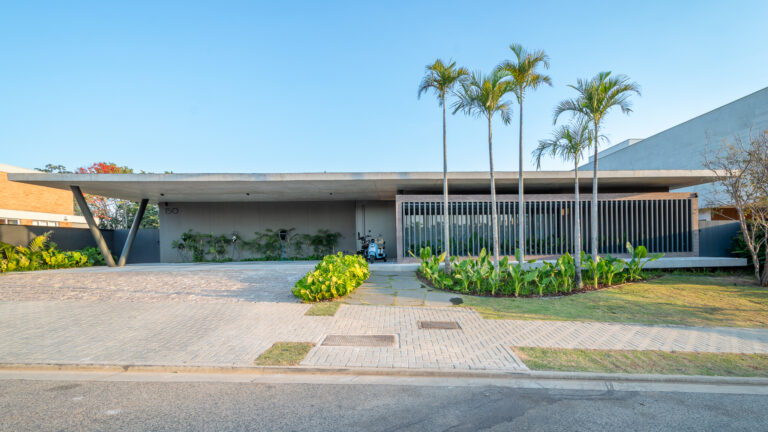Fachada de residência térrea contemporânea com laje de concreto em balanço sobre pilares inclinados e jardim tropical
