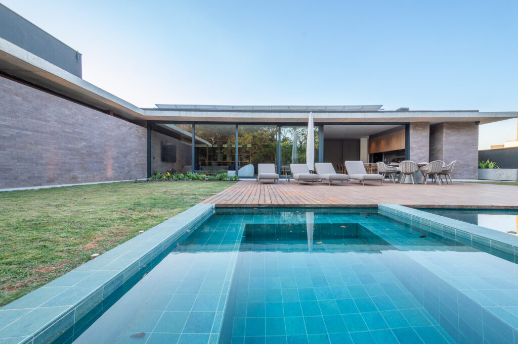 Fachada dos fundos com piscina, deck de madeira, paredes de tijolo e panos de vidro Weiku de perfil escuro
