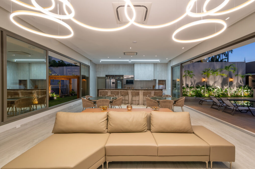 Espaço gourmet à noite com portas de vidro de correr Weiku totalmente abertas para a piscina e o jardim iluminado