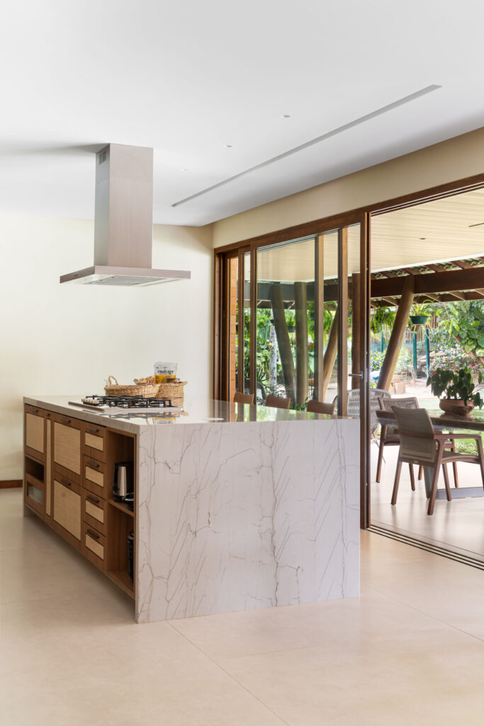 Cozinha com ilha em pedra e portas de vidro de correr Weiku de grande vão abertas para a varanda e o jardim