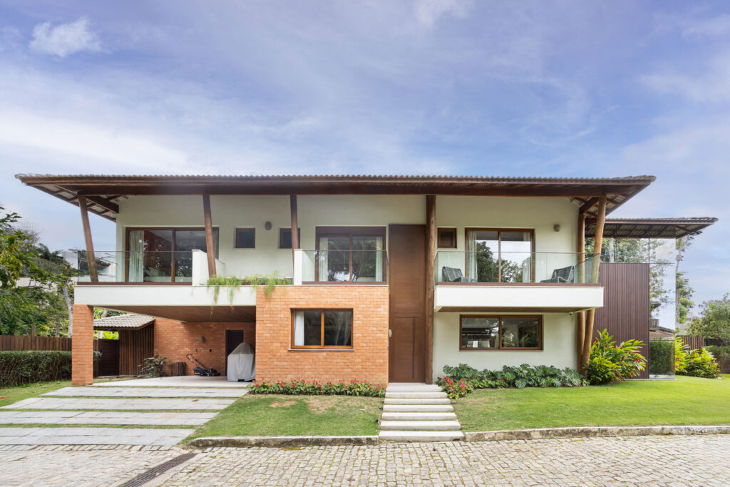 Fachada dos fundos de residência tropical com varandas, pilares de madeira, telhado cerâmico e esquadrias de vidro Weiku abertas para o jardim