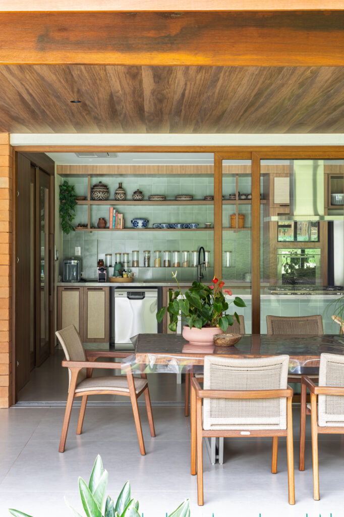 Varanda gourmet com mesa de madeira integrada à cozinha por portas de vidro de correr Weiku