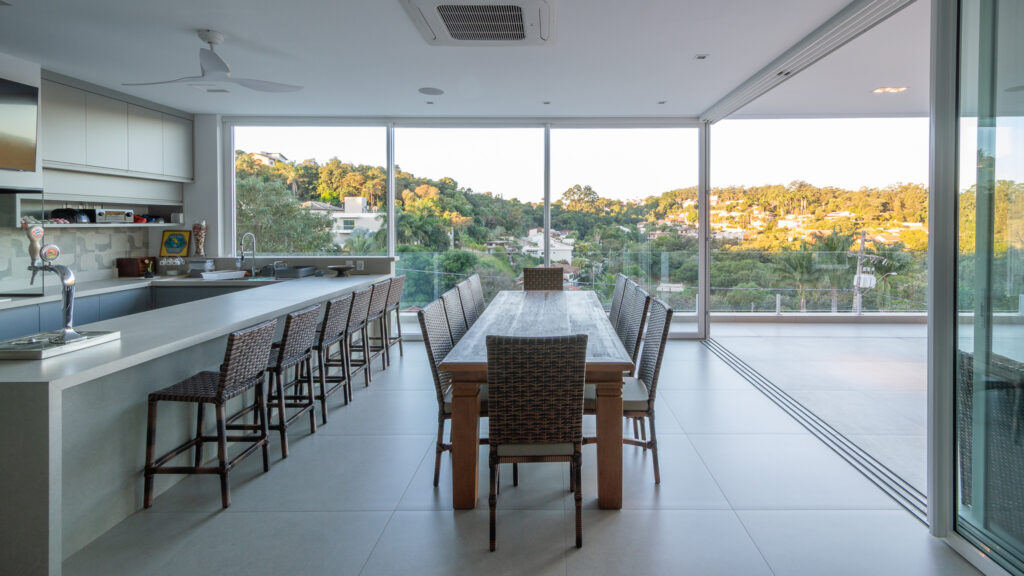 Espaço gourmet com bancada e mesa de jantar, com portas de vidro de correr Weiku abertas para a varanda e a vista