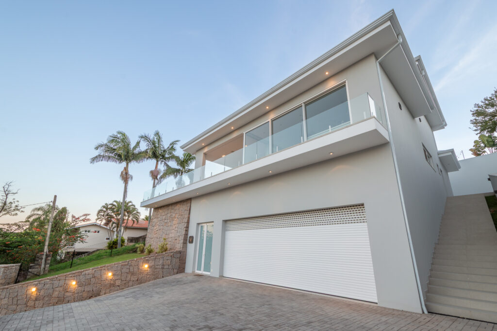 Fachada de acesso com base em pedra, garagem e varanda superior com panos de vidro Weiku e guarda-corpo de vidro